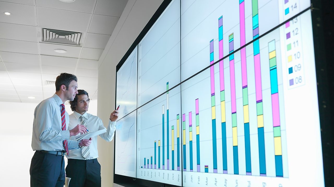 Business men analyse reports displayed on a large digital screen