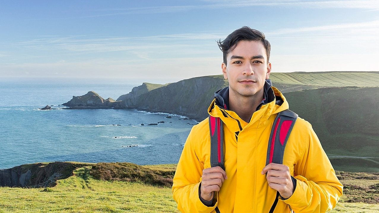 Young man standing on cliff side overlooking a calm sea