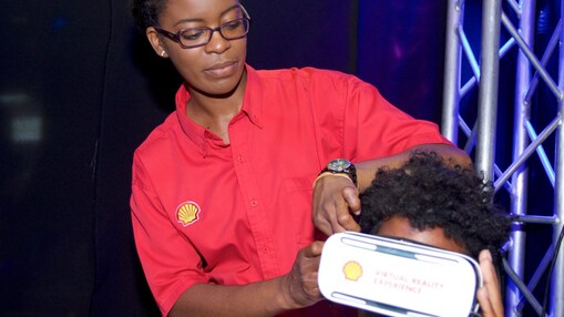 Woman wearing a red shirt with Shell logo helps a visitor wear AR goggles at an event