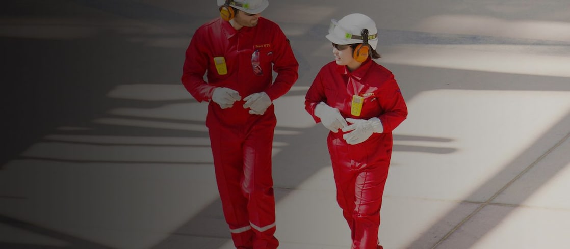 Male and female worker in red overalls and white helmets and hearing protection walking
