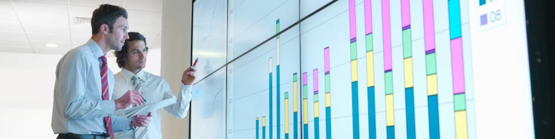 Business men analyse reports displayed on a large digital screen