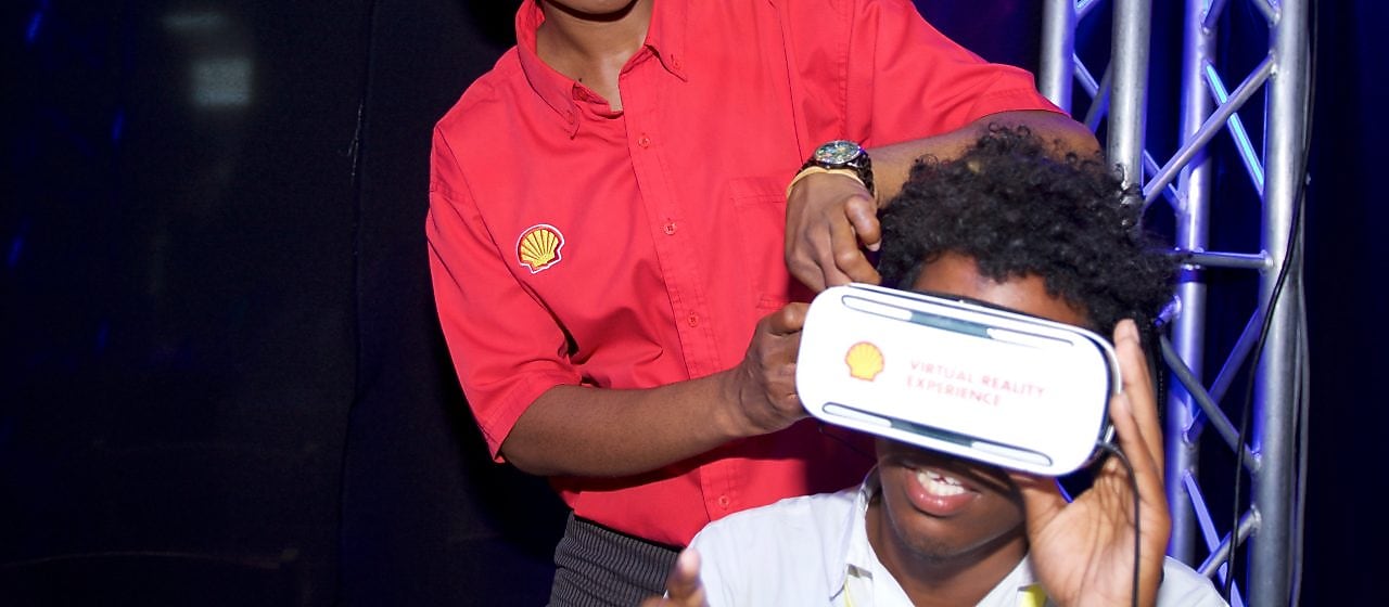 Woman wearing a red shirt with Shell logo helps a visitor wear AR goggles at an event