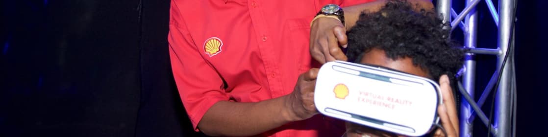Woman wearing a red shirt with Shell logo helps a visitor wear AR goggles at an event